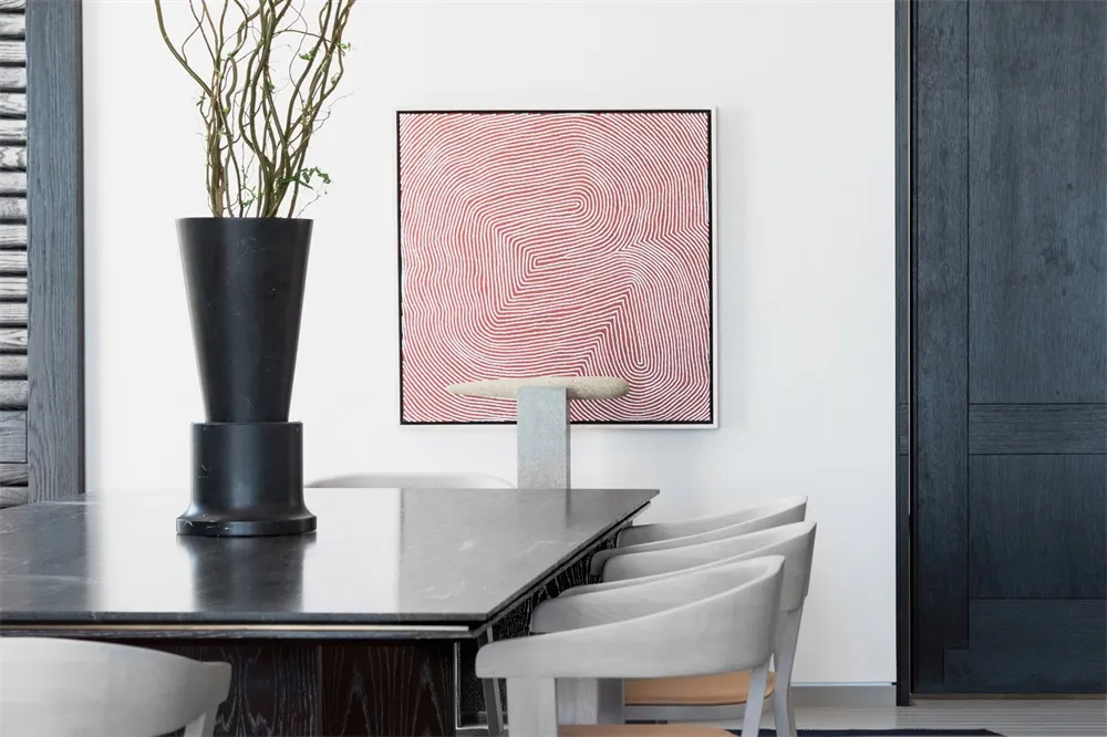 A modern dining table made of concrete with white chairs and a red and white abstract painting.