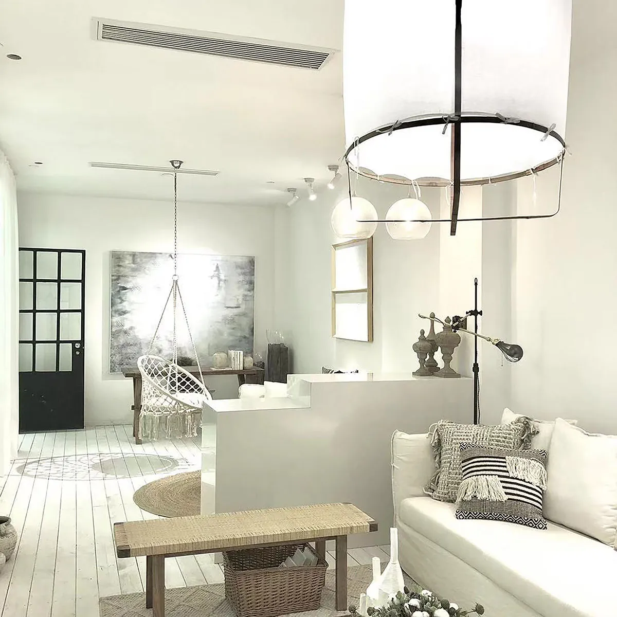Minimalist living room with white and neutral color palette, featuring white couch, hanging chair, and modern lighting fixtur