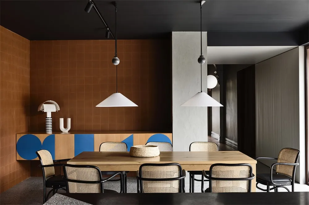 Modern dining room featuring a wooden table with cane chairs and pendant lighting.