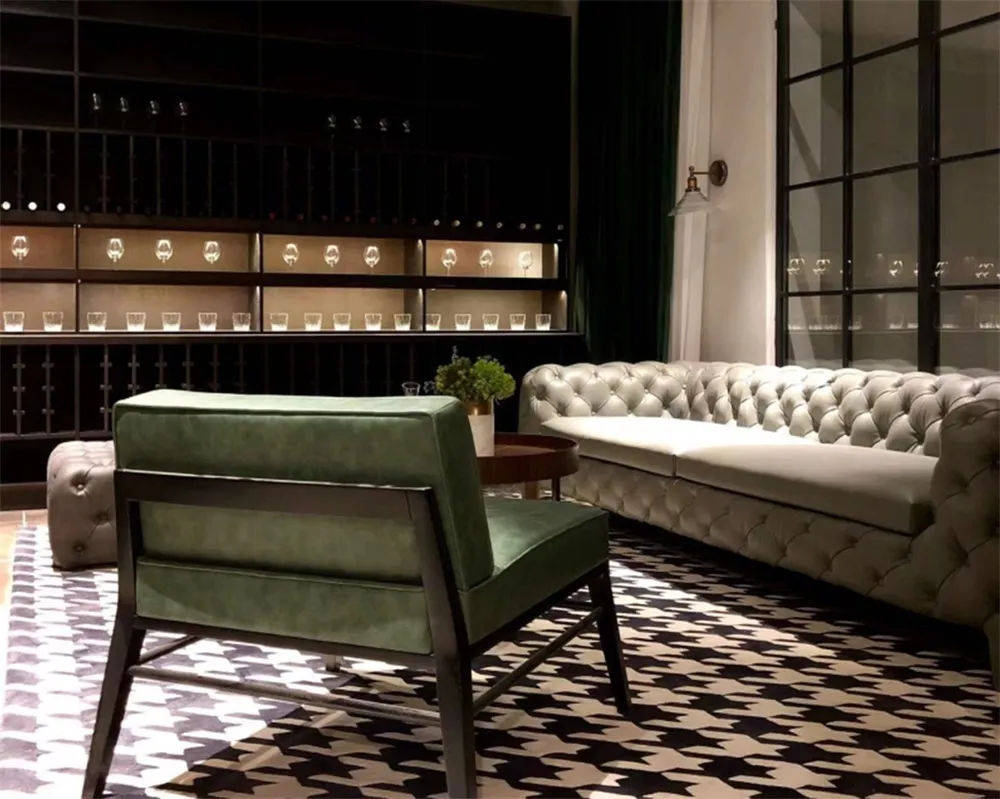 A modern living room with a green armchair, white tufted sofa, and black and white patterned rug.