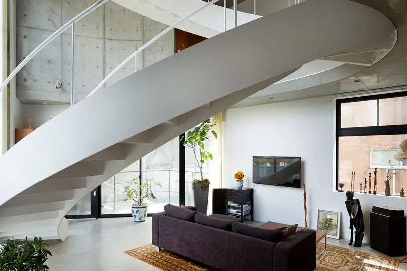 A modern, minimalist living room with concrete walls, a glass staircase, and a steel beam ladder.