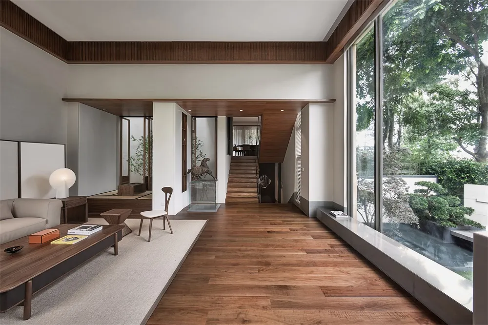 A modern minimalist living room with wooden flooring and white walls, featuring a sofa, coffee table, bookshelf, and a view o