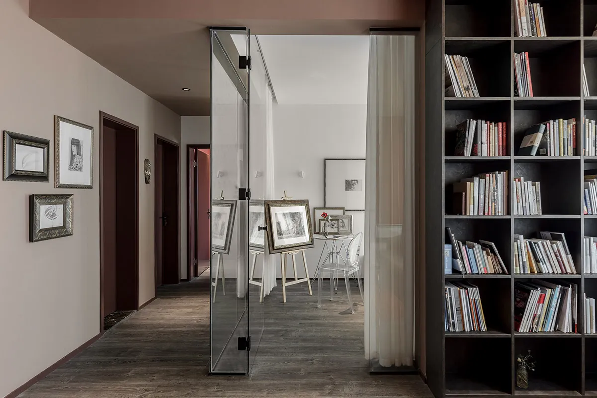 A minimalist home library with dark stone walls, a large bookshelf, and framed artwork.