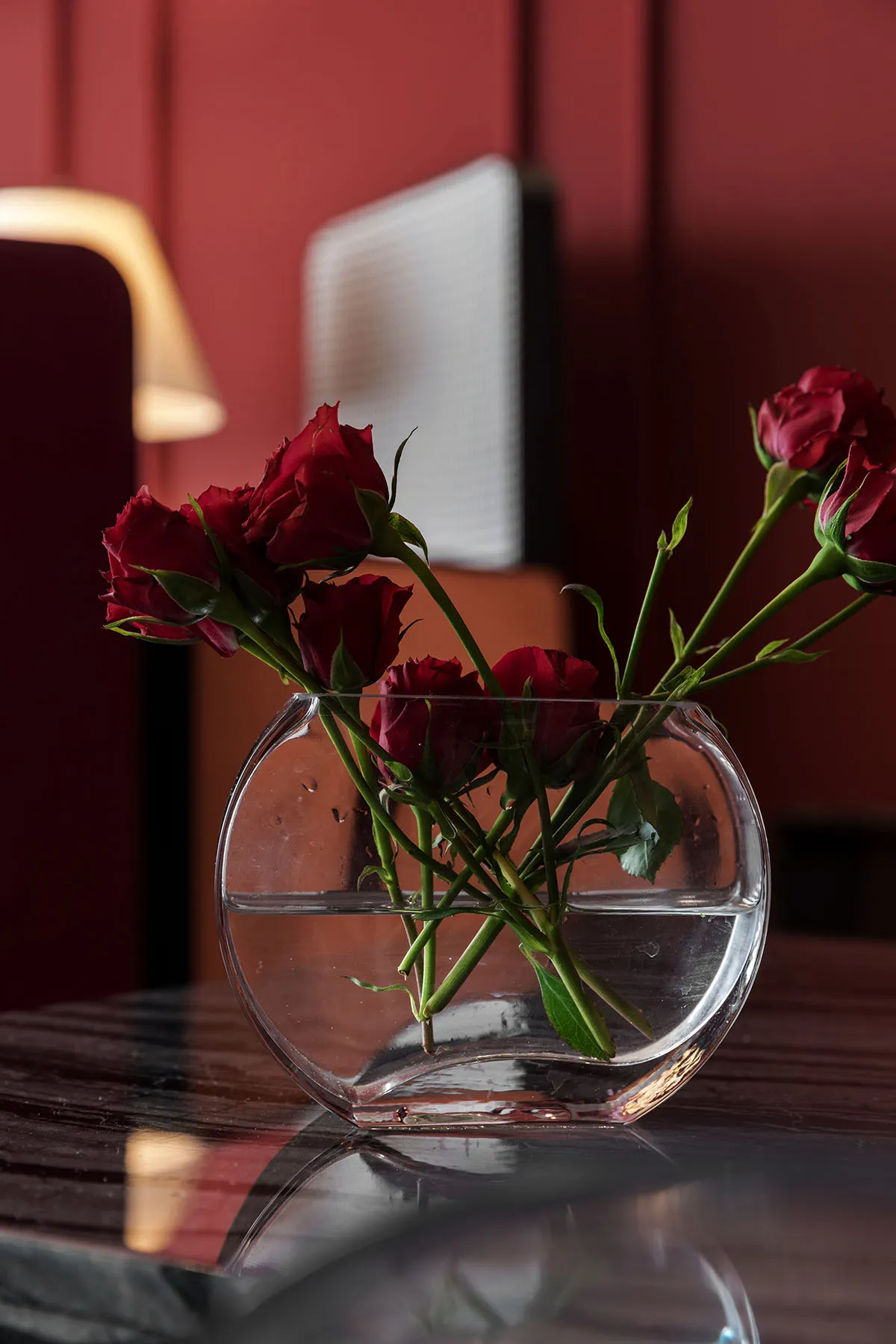 A transparent glass vase containing several red roses on a reflective surface.