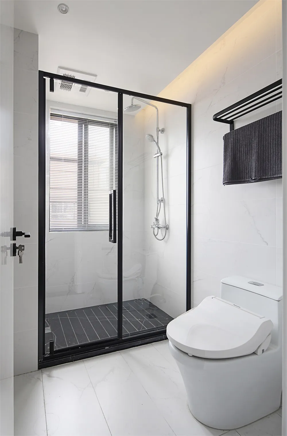 Modern minimalist bathroom with white marble tiles, glass shower enclosure, and black fixtures