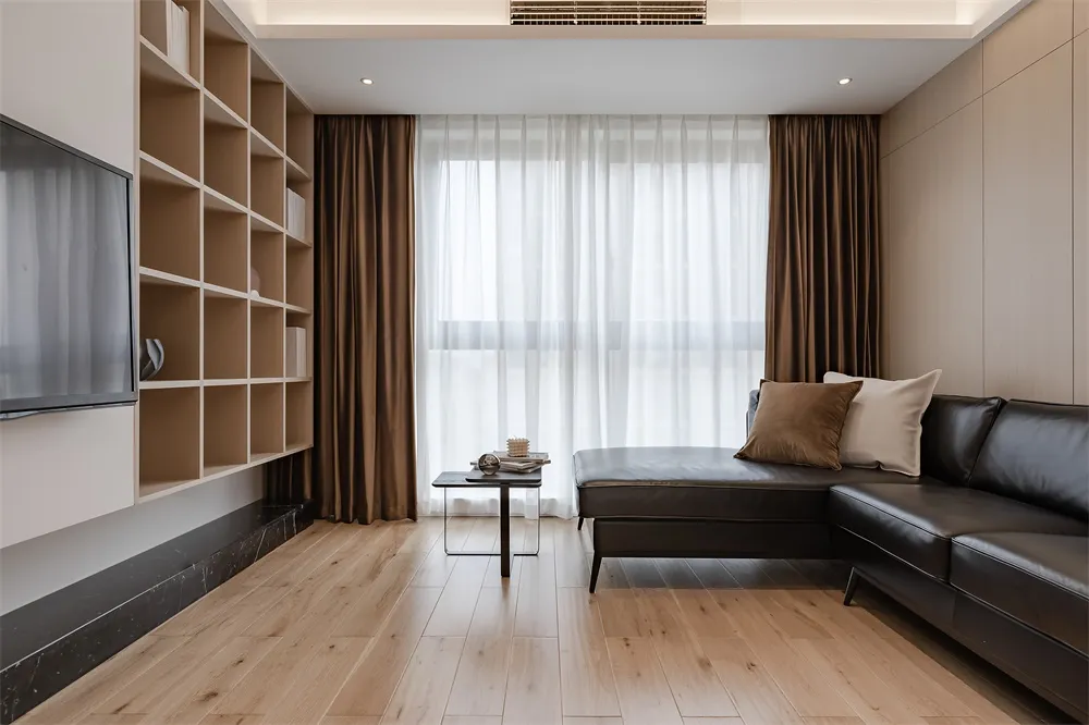 Modern minimalist living room with wooden floors, black leather sofa, and bookshelf