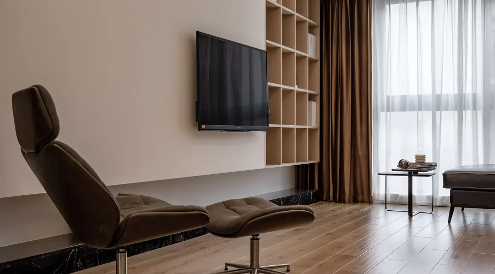 Modern living room with a brown leather lounge chair, wooden flooring, and a wall-mounted TV.