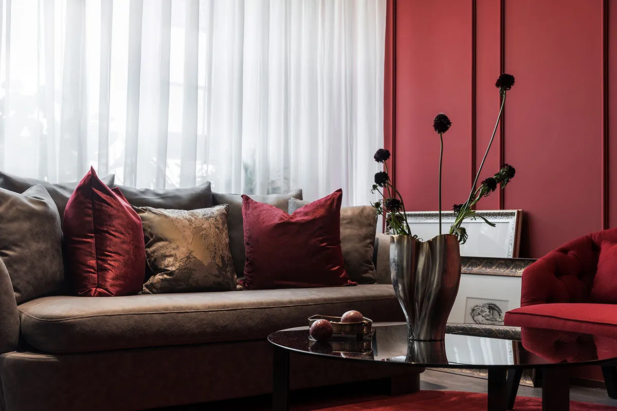 A modern living room featuring cushions in various shades of red and gold, a round glass table, and a red armchair.