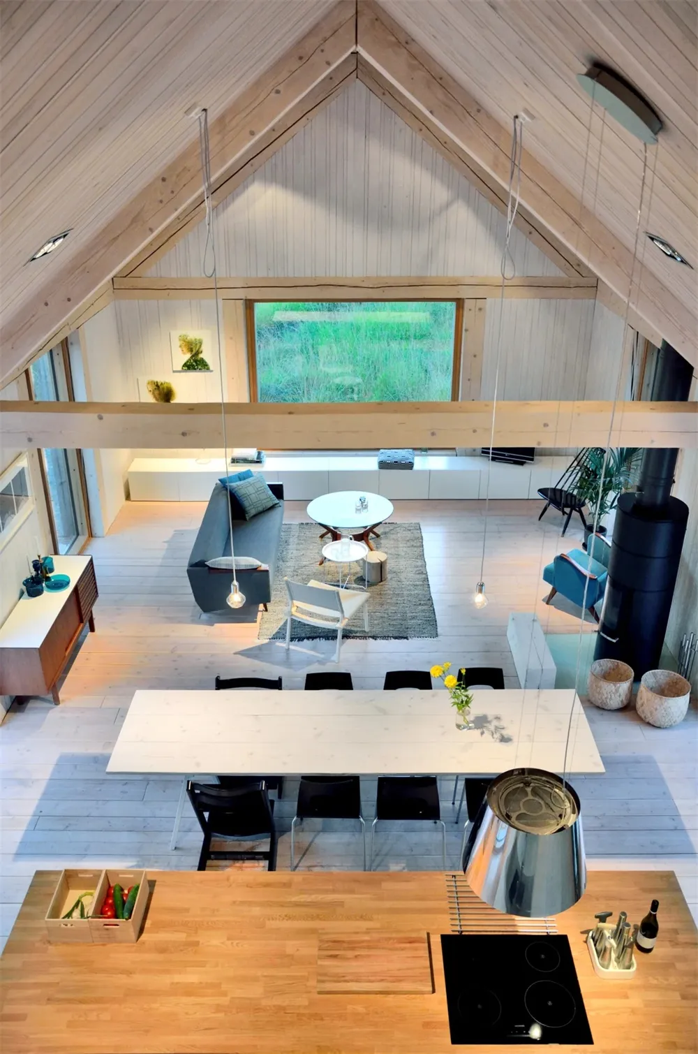 A modern minimalist living, dining, and kitchen space with a high-vaulted ceiling, wooden beams, and white furnishings.