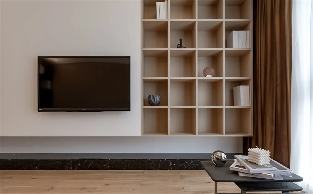 Modern minimalist living room with a flat-screen TV mounted on the wall, a wooden floor, and a black coffee table with books
