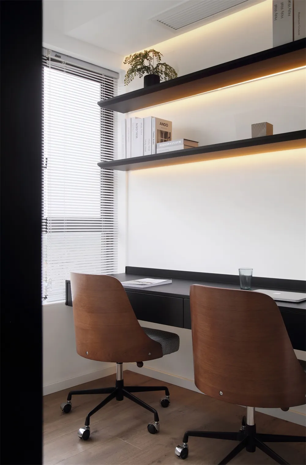 A modern office space featuring wooden accents, minimalist design, and a sleek desk setup with shelves and books.