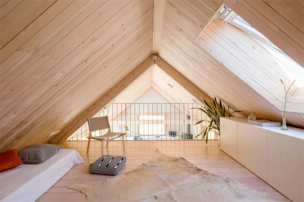 A minimalist attic bedroom with wooden floors, a bed, a chair, a cabinet, and a window providing natural light.