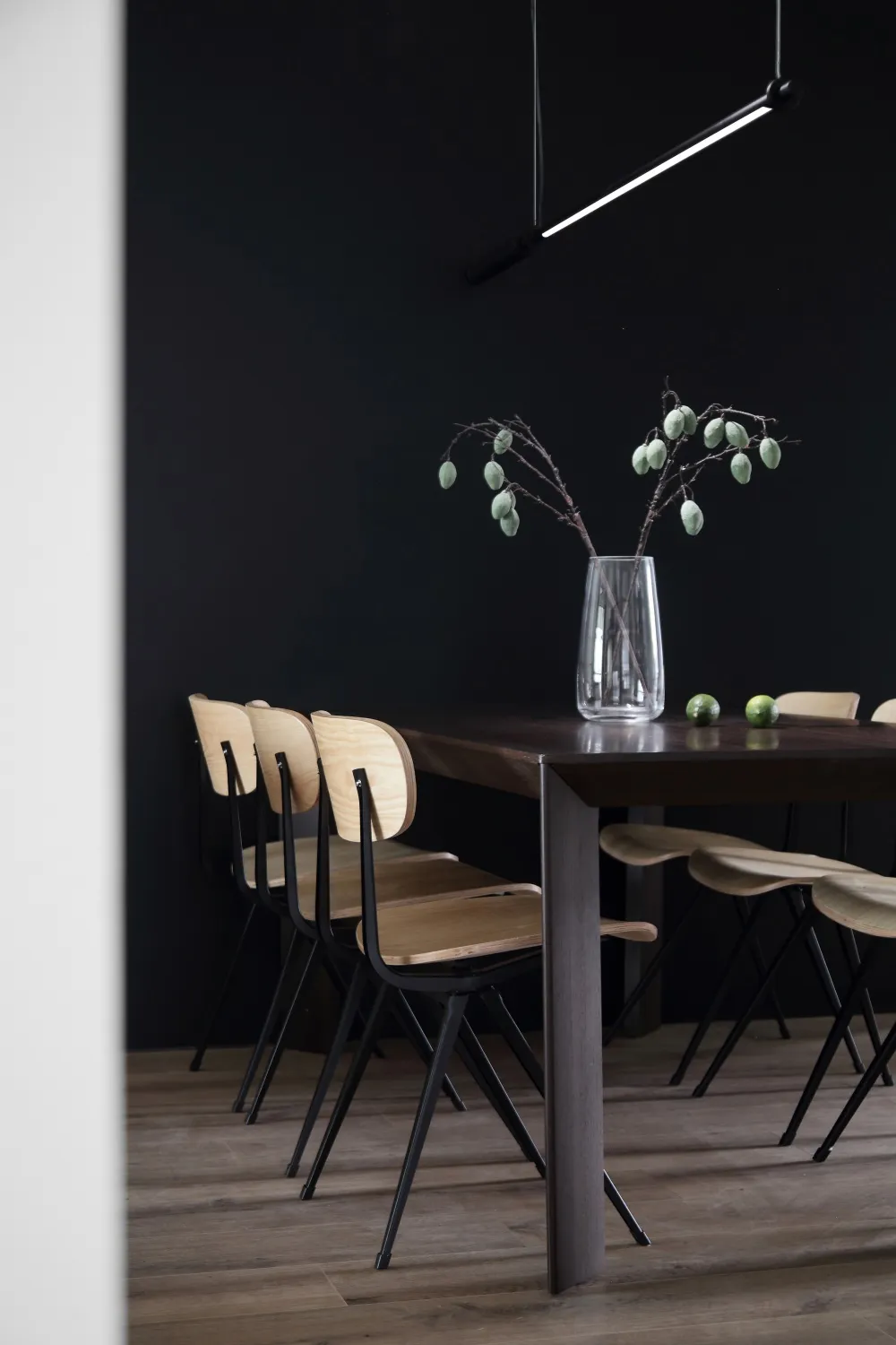 A minimalist dining room featuring wooden furniture and a dark wall.