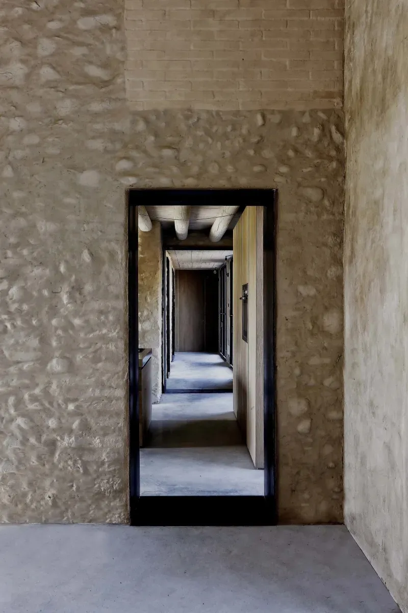 A modern corridor features concrete and brick walls with a stone accent, leading to a hallway with a wooden floor and a stone