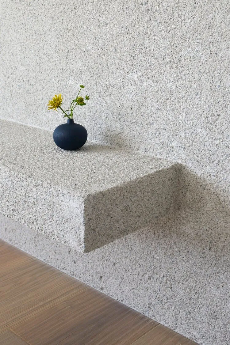 A minimalist concrete shelf featuring a black vase with a single flower arrangement.
