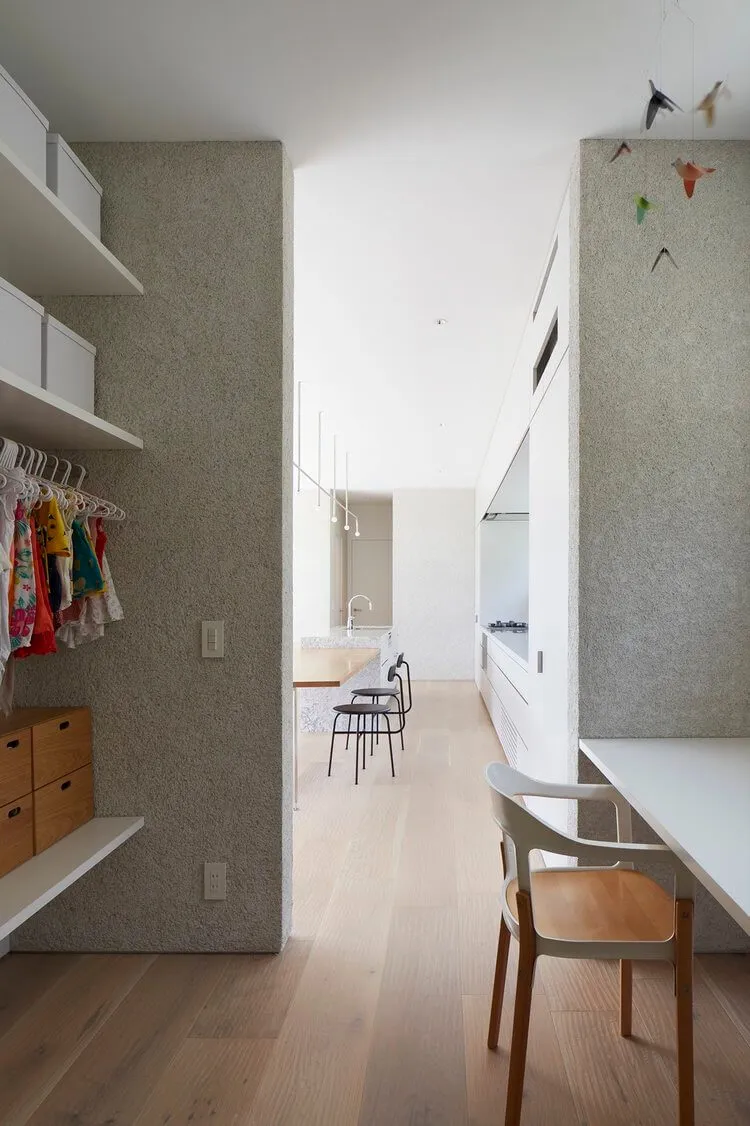 Modern minimalist kitchen with concrete walls, wooden flooring, and a long dining table.