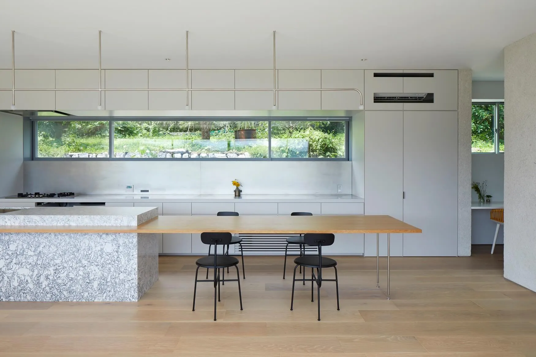 Modern kitchen with minimalist design, marble countertops, stainless steel appliances, and large windows overlooking greenery
