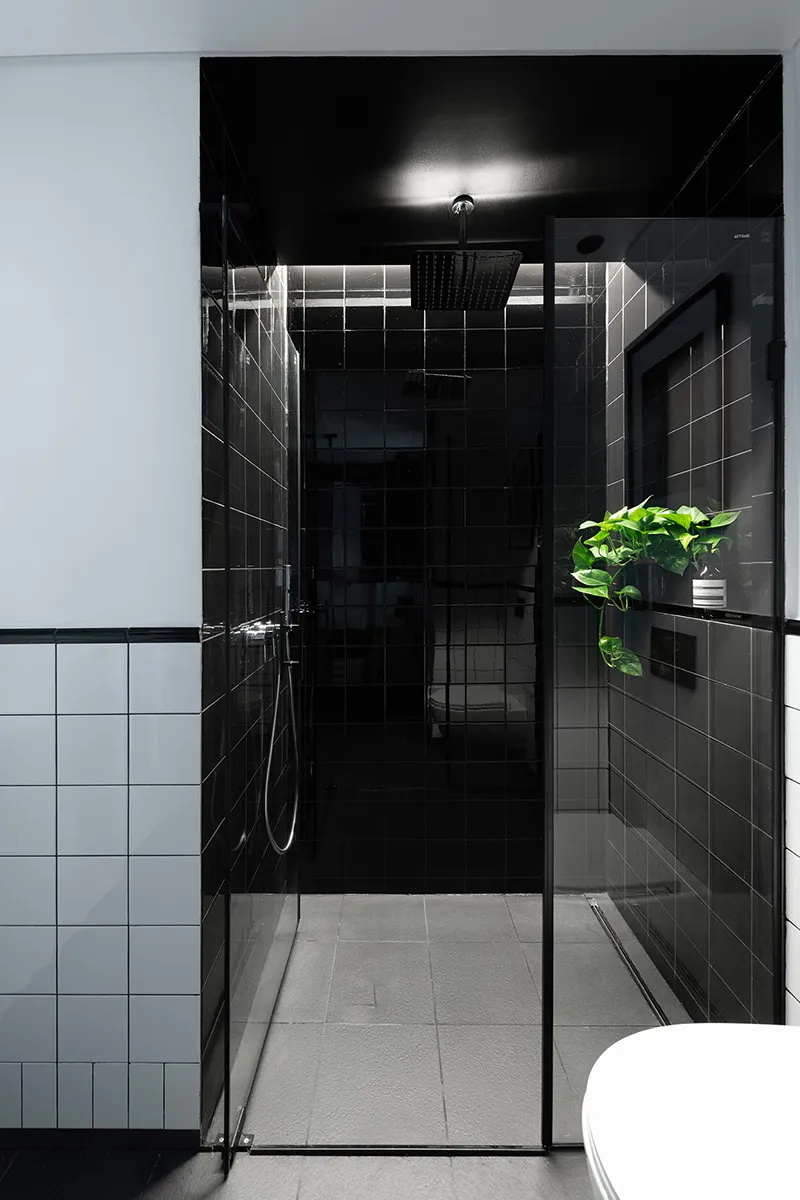 A sleek modern bathroom with black tiled walls and a glass shower enclosure, featuring a white toilet in the foreground and a