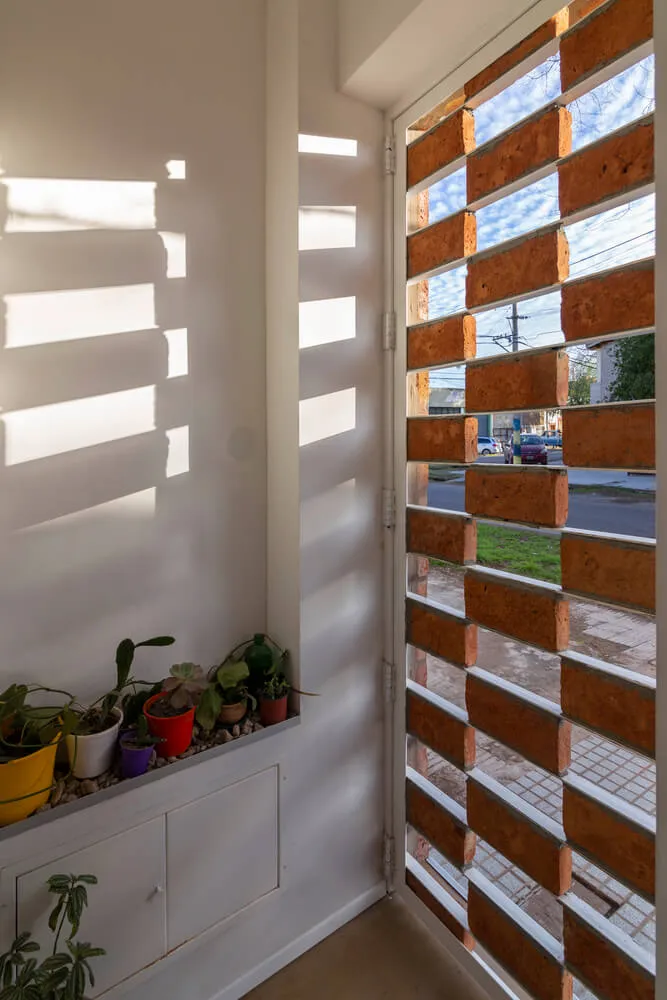 A modern residential interior featuring brick window shutters and a white wall with sunlight casting shadows.