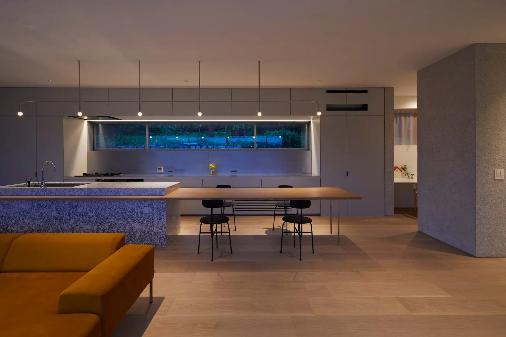 A modern kitchen and dining room with a marble island, wooden dining table, and concrete and glass finishes.