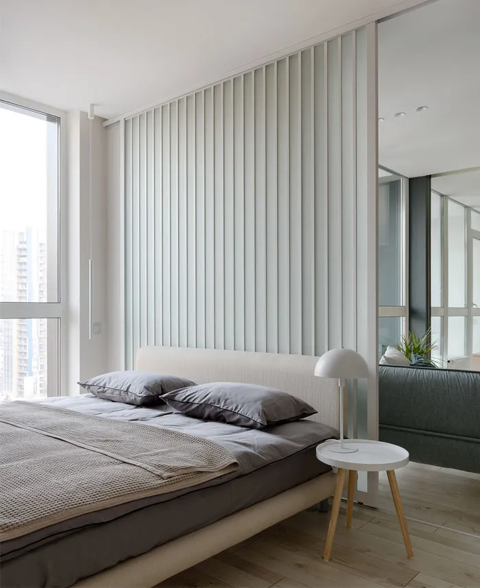 Modern minimalist bedroom with a neutral color palette, including a bed with a white headboard and grey linens, a white side