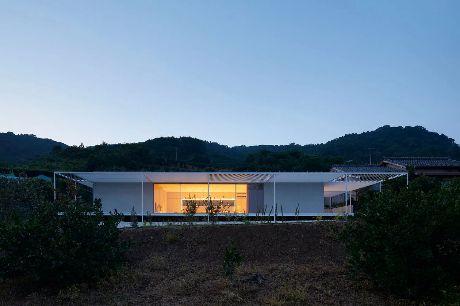 Modern minimalist concrete house at dusk with illuminated interior.