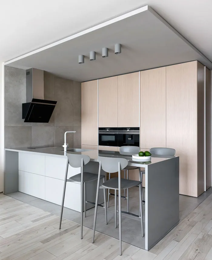 Minimalist residential kitchen with concrete countertops, light wood cabinets, and metallic stools on a wooden floor.