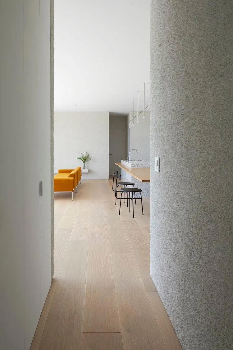 Modern minimalist living room with light wood flooring, a yellow sofa, and a grey textured wall.
