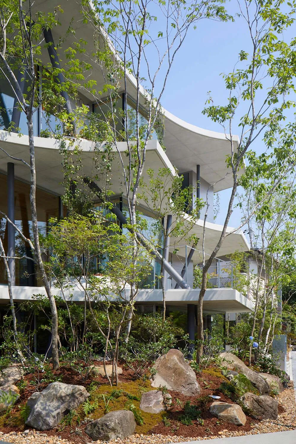 一座現代住宅建築,外牆採用混凝土與玻璃材質,周圍環繞綠意與岩石。