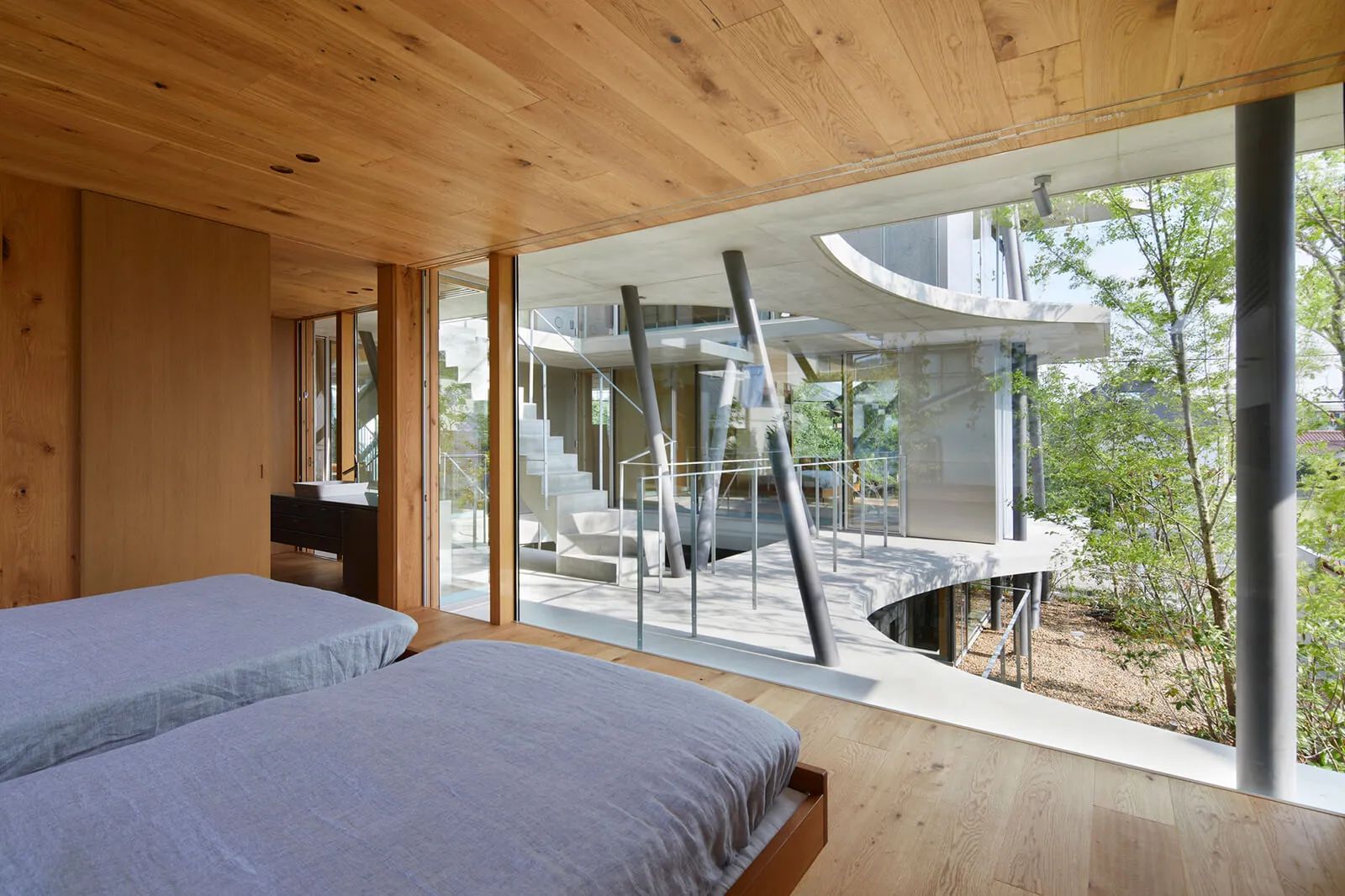 Modern bedroom with wooden floors and furniture, featuring a glass wall and a staircase.