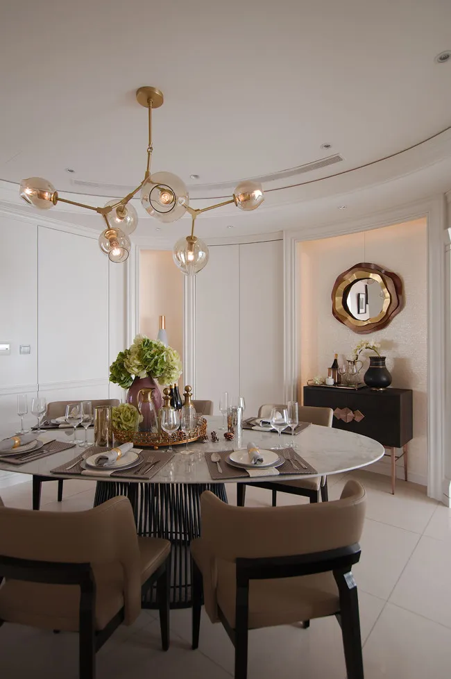 Modern dining room featuring a circular marble table, upholstered beige chairs, and a stylish brass chandelier with multiple