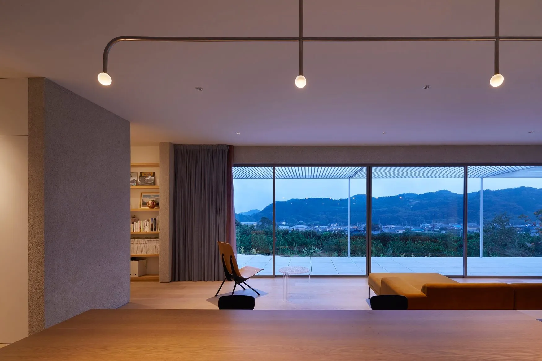 Modern living room with large windows offering a view of mountains and buildings at dusk.