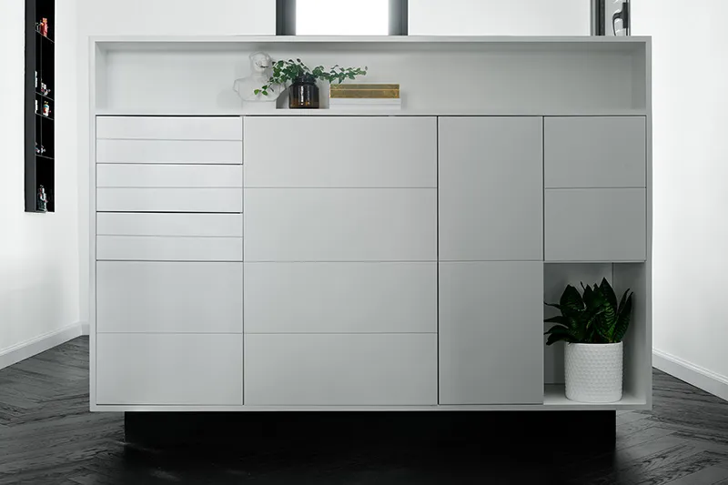 A modern, minimalist white concrete storage unit with three drawers, four doors, and open shelving.