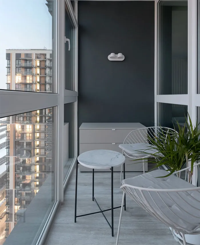 Modern balcony featuring marble side table and metallic chairs beside a glass window.