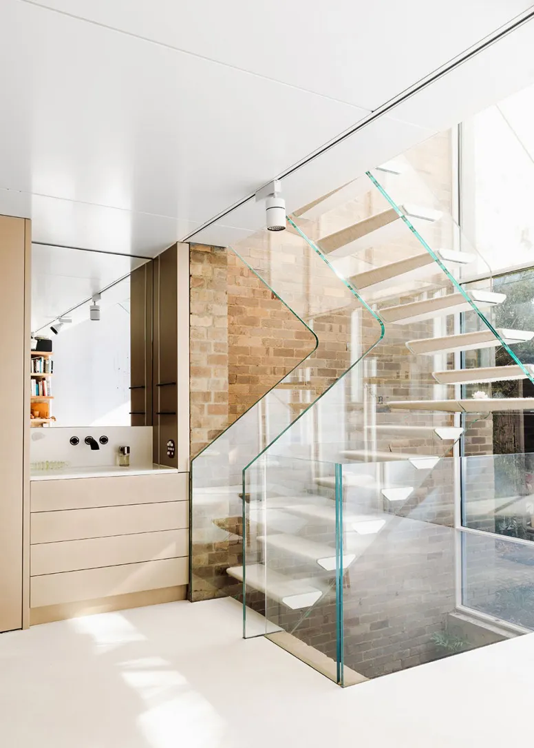 Modern, industrial-style staircase with transparent glass balustrade and white flooring.
