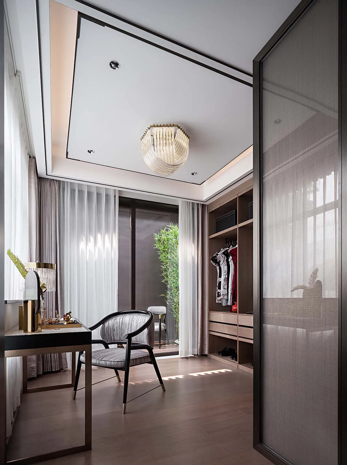 A modern luxury walk-in closet featuring a wooden floor, glass doors, and fabric drapes.