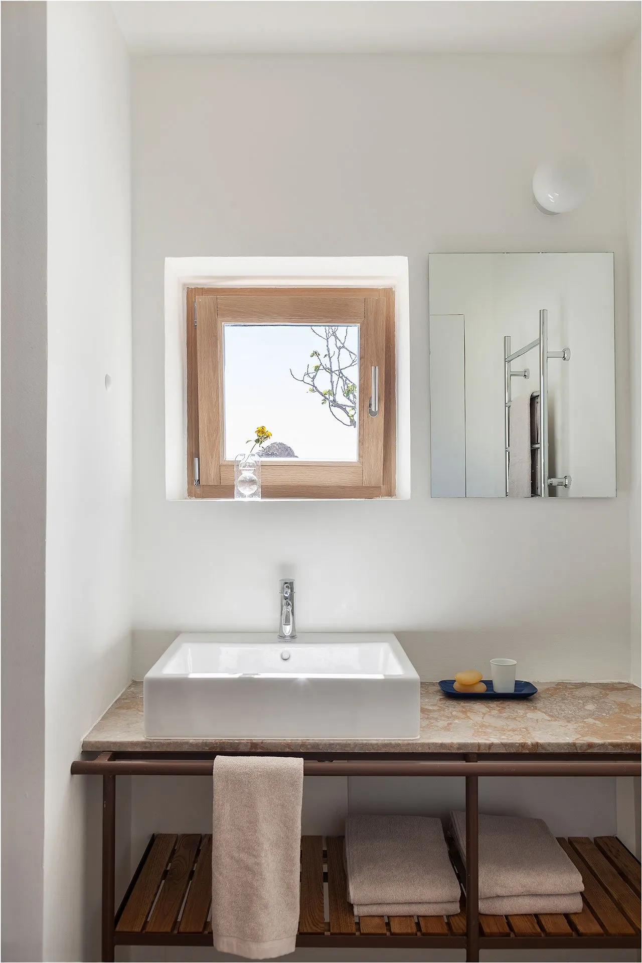 A minimalist bathroom features a white concrete sink, a marble countertop, and a metal faucet, with a small window and a mirr