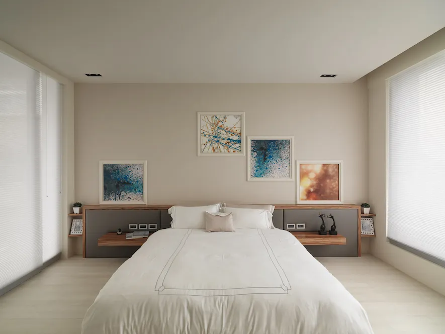 Modern minimalist bedroom with a white bed, white bedding, and abstract paintings on the wall.