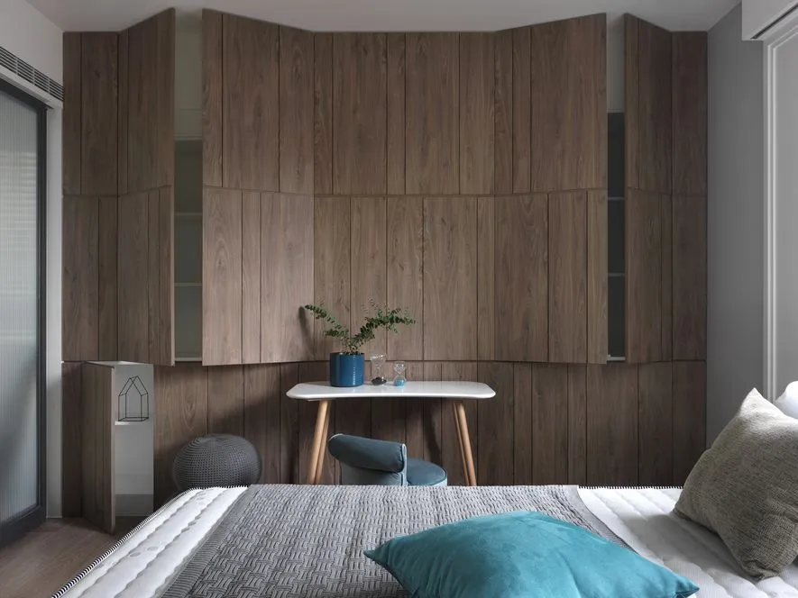 A modern minimalist bedroom with wooden walls and a white desk with a green plant and a blue vase.