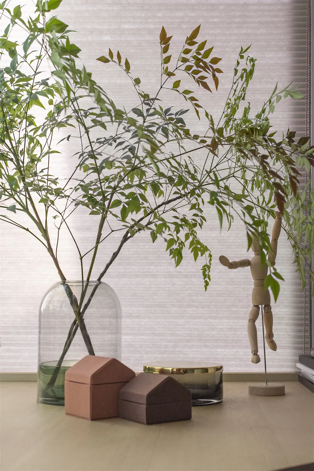現代裝飾花盆，置有綠葉與小屋造型盒子，擺放在木質表面上。