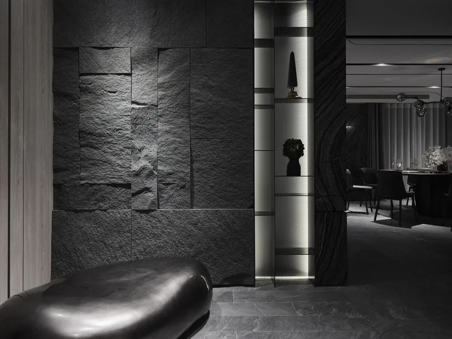 A minimalist black and white scene featuring textured black metal furniture against a textured black wall.