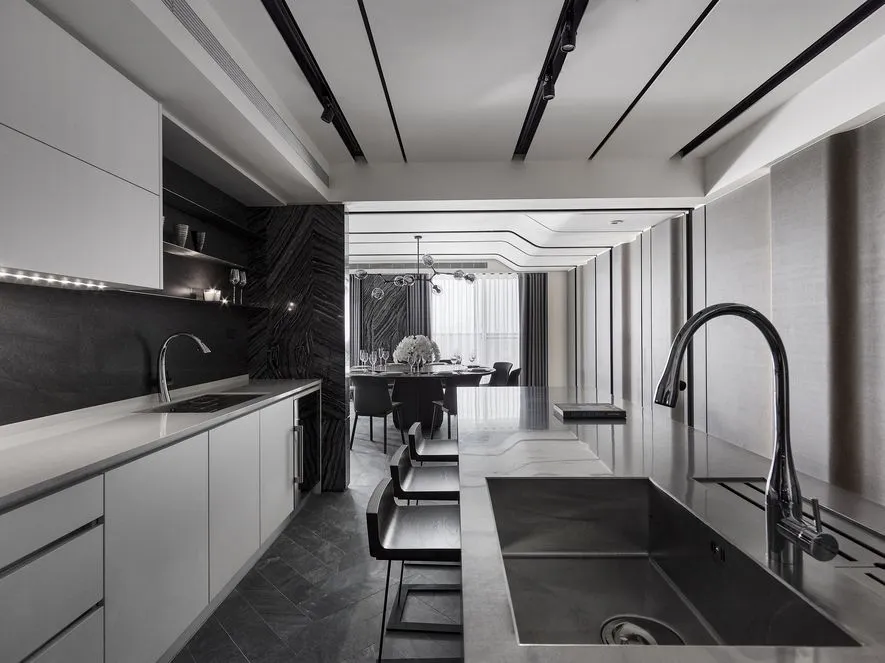 A sleek, modern kitchen with metallic black finishes, white countertops, and a large island.