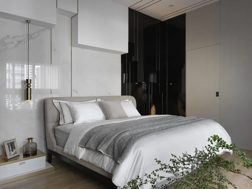 A modern minimalist bedroom with a white marble accent wall, metal headboard, and a grey bedspread.
