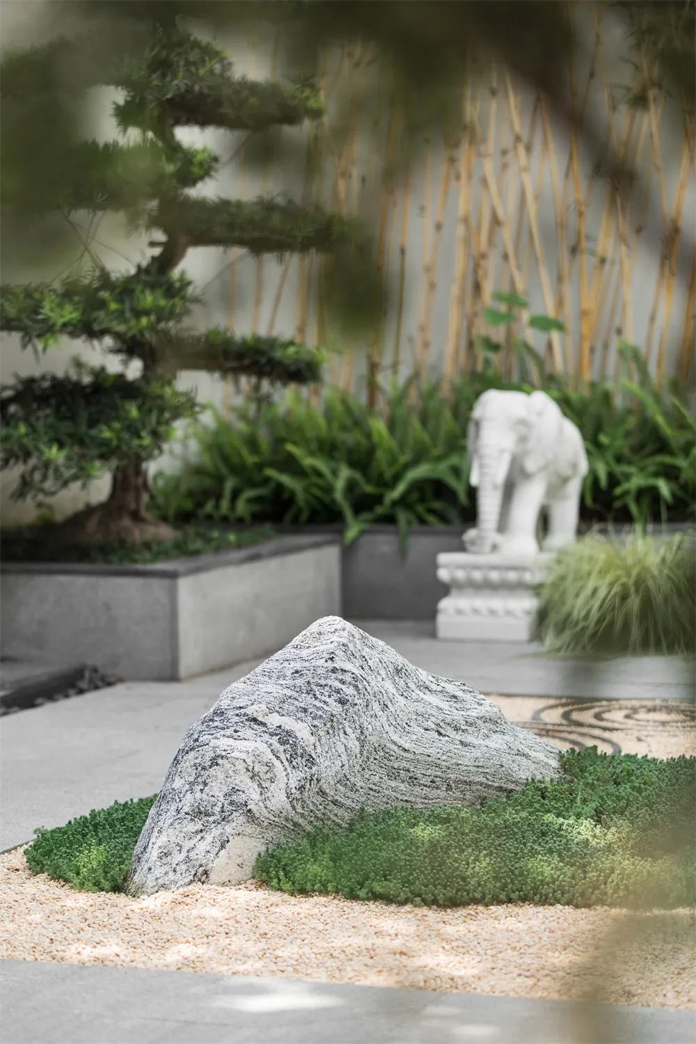 A modern landscape design featuring granite rock, gravel bed, and lush green plants.