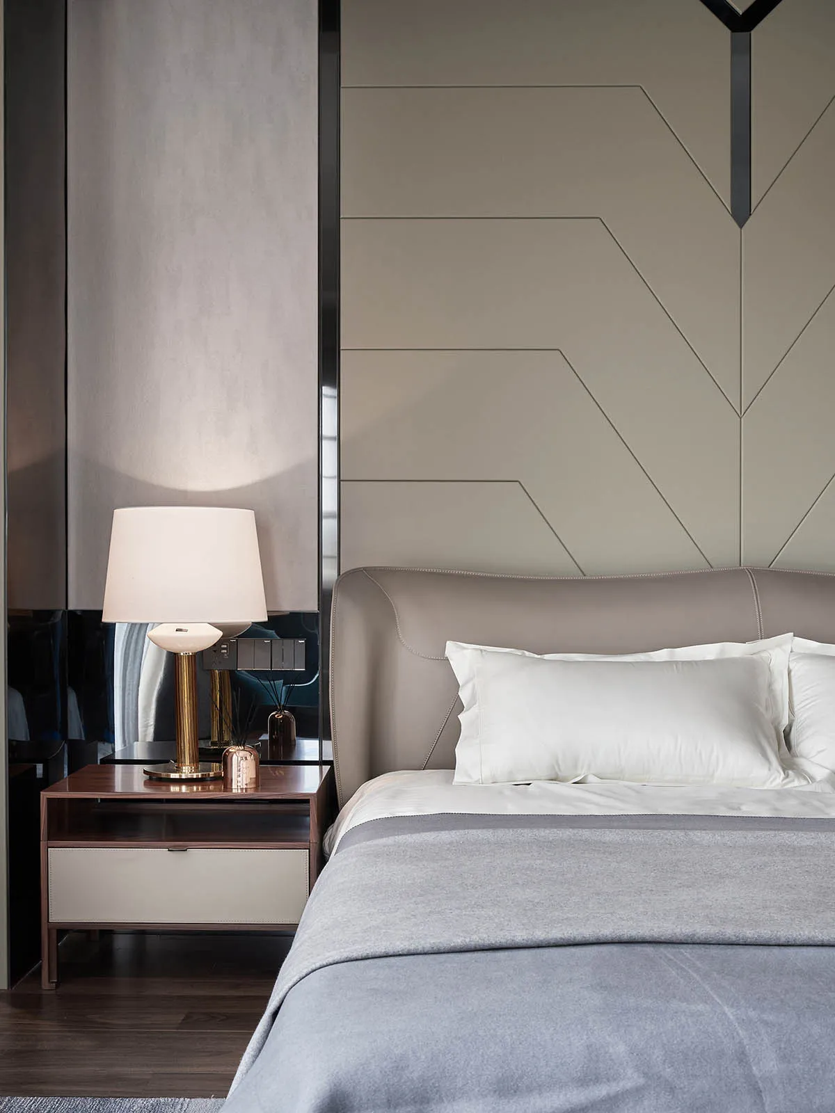 A minimalist bedroom with neutral-toned materials, showcasing a bed with white pillows and a gray blanket, accompanied by a m