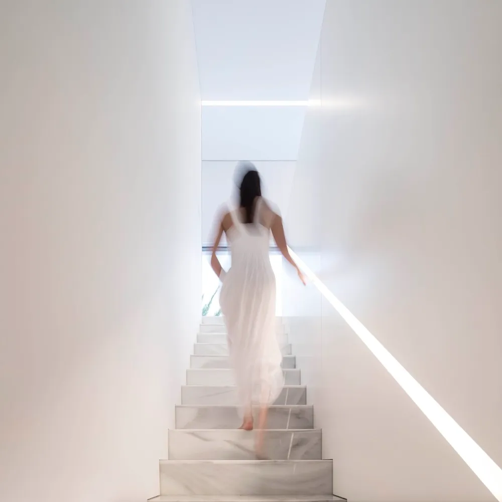 A woman in a white dress walking up a staircase made of white marble.