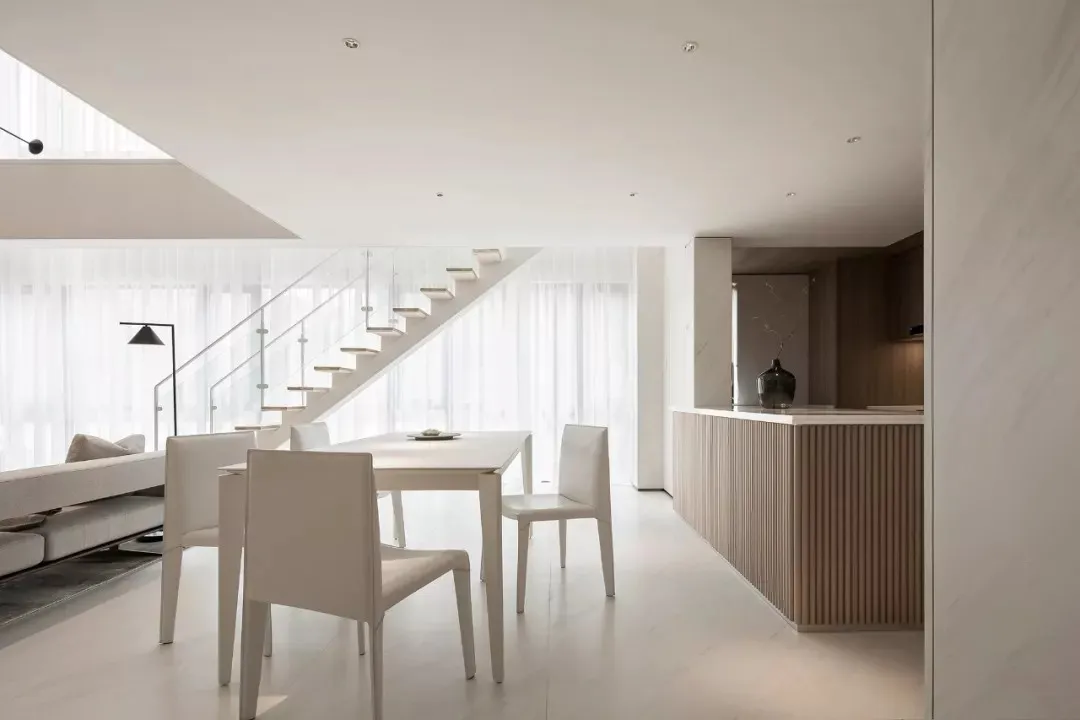 Modern minimalist residential interior with white furniture, wooden accents, and a light-filled space.