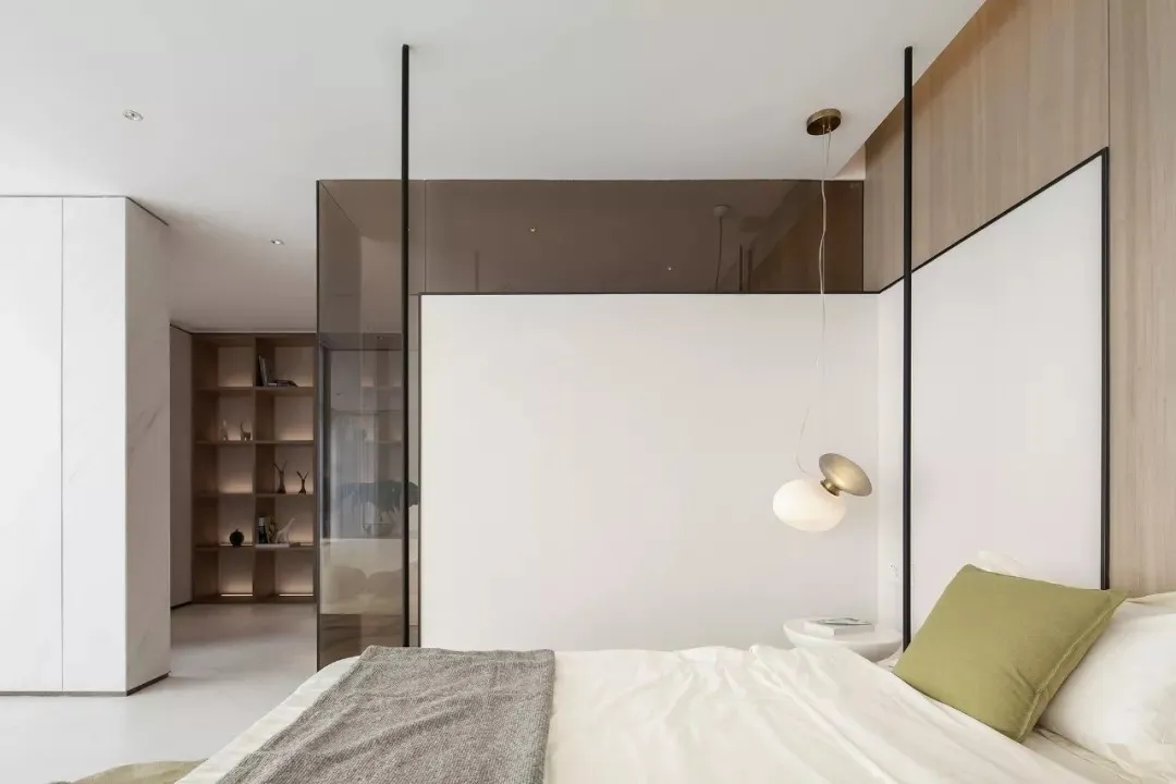 A minimalist bedroom with white walls, a bed, green pillow, and a glass partition.
