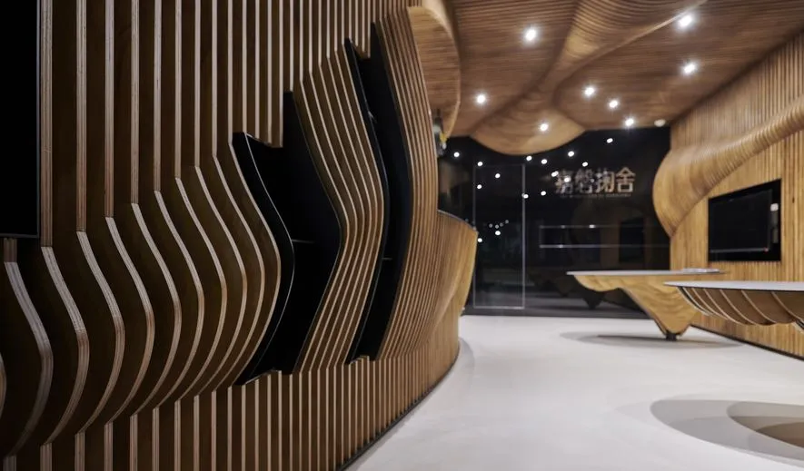 Modern lobby featuring textured wooden walls and curved wooden furniture against a white floor.