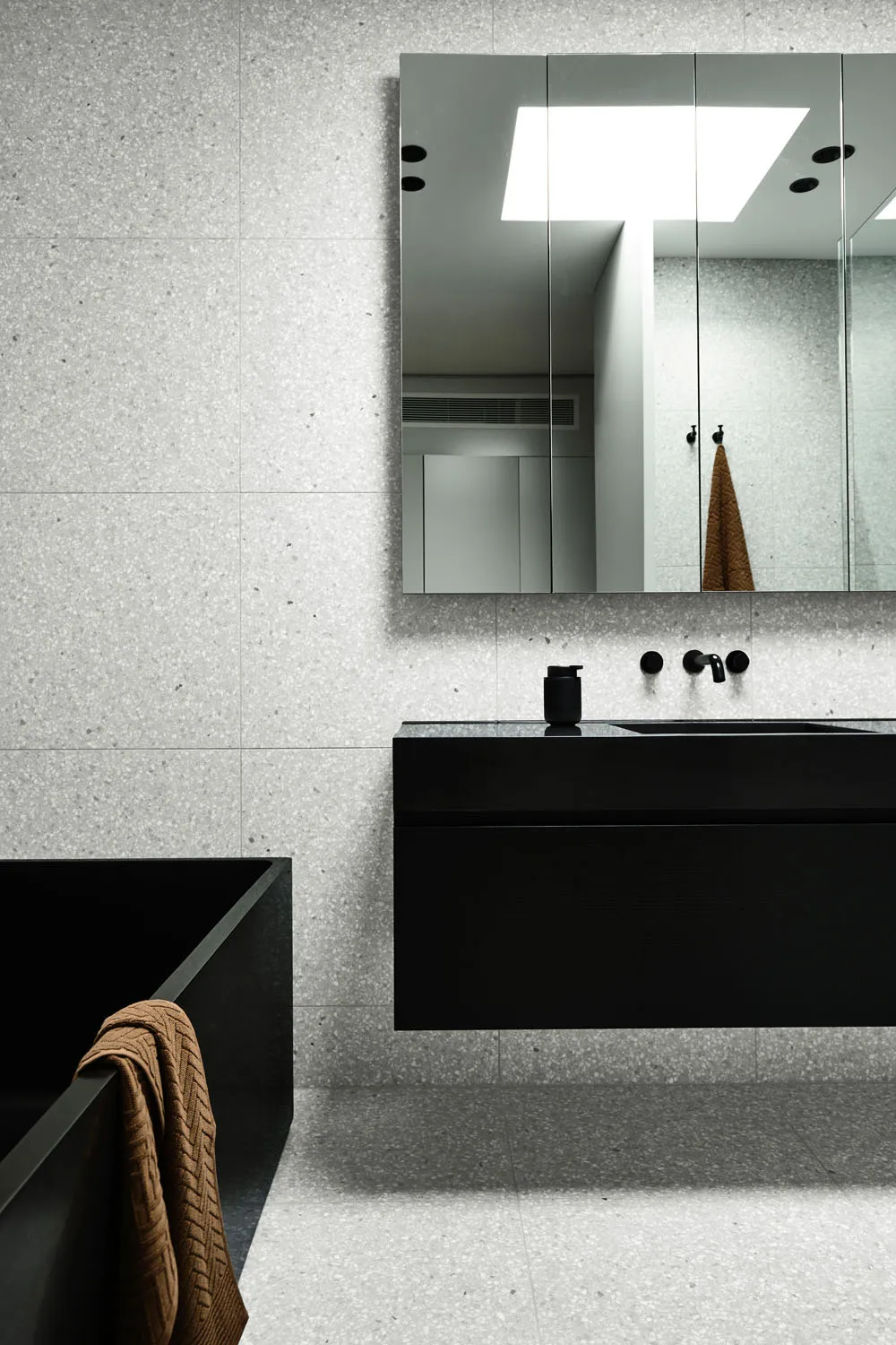 Minimalist bathroom with black and white elements, including a floating vanity, concrete walls, and a terrazzo floor.